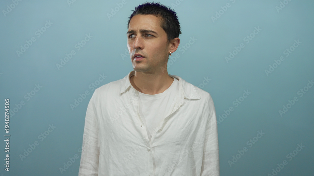 Obraz premium Young hispanic man in white shirt stands isolated against a blue background wall, expressing curiosity with a thoughtful pose and a pensive facial expression.