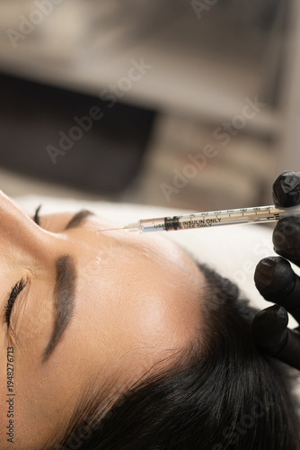 Woman getting botox injection into forehead by gloved hand for skin rejuvenation