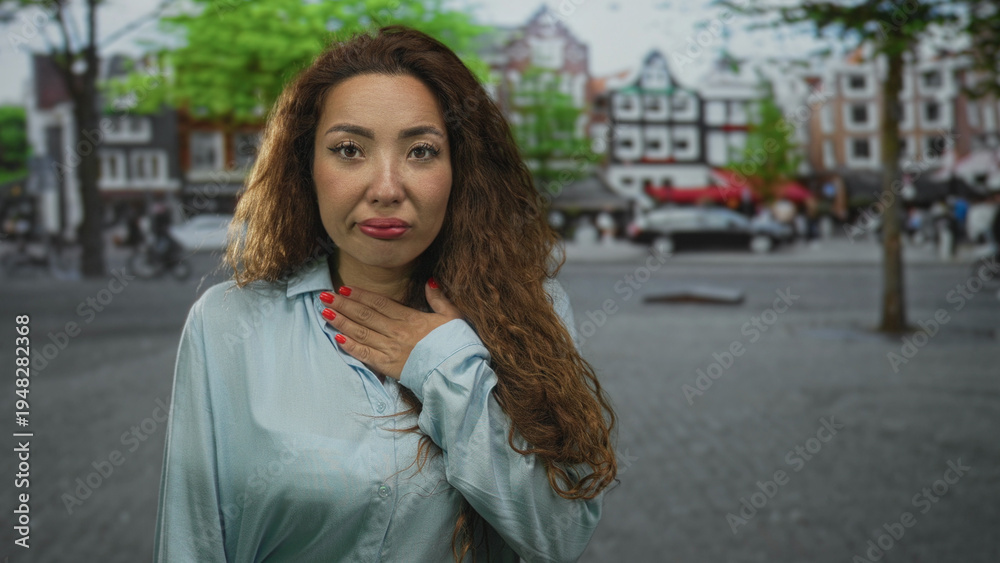 Fototapeta premium Woman with hand on chest on a street, red nails visible and uneasy expression; concern vulnerability.