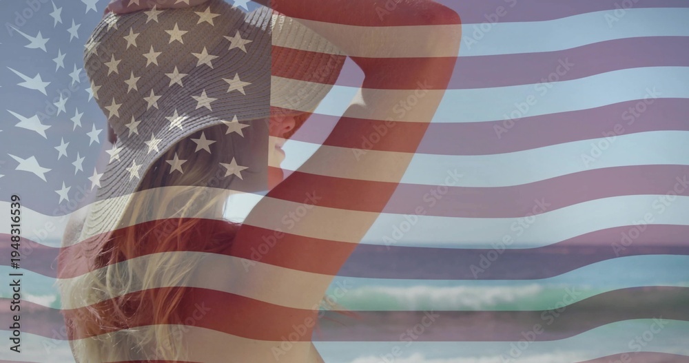 Fototapeta premium Standing woman watching waves at beach, wearing straw hat, swimsuit, US flag overlay, copy space
