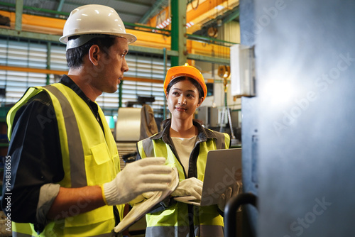 Australian male engineer and Asian female engineer collaborating on CNC machine operation and technical data analysis using a laptop on the factory floor.