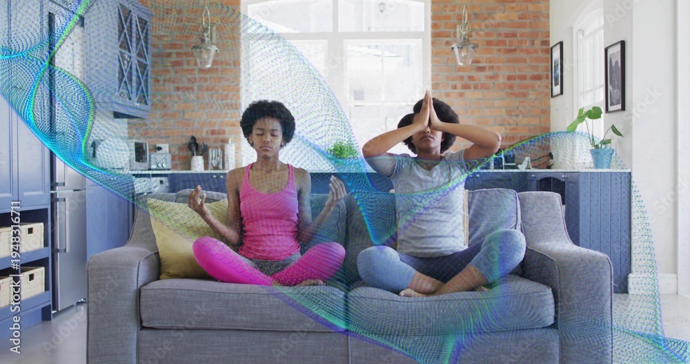 Fototapeta premium Meditating mother-daughter sitting on grey sofa in home kitchen in pink and grey with teal overlay