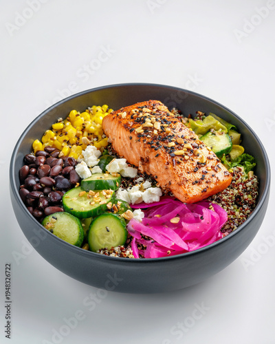 A buddha bowl made with cooked  quinoa, roasted corn kernels, cooked black beans, diced Persian cucumbers, pickled red onions, grilled salmon fillet and queso fresco chunks 