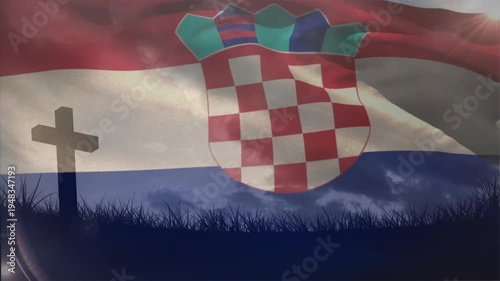 Flag waving, breeze causing checker shield folds and sun flare shifting over cross memorial