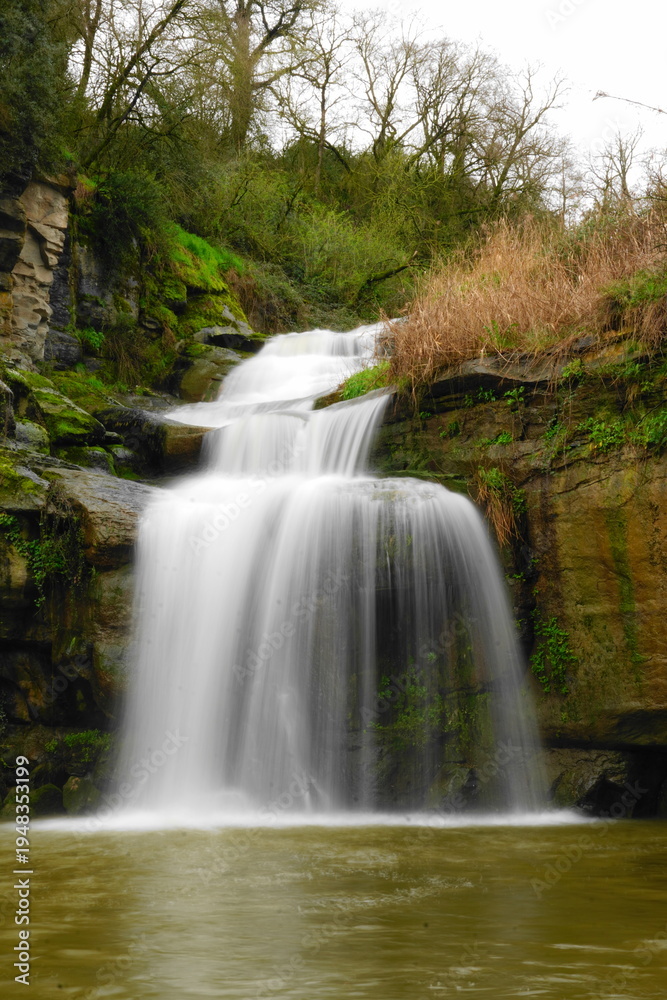 Fototapeta premium Silky waterfall in lush forest with mossy rocks and flowing stream, long exposure nature landscape