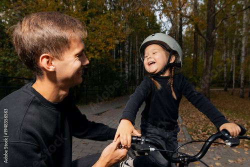 Obraz na plátně Father teaches daughter to ride bicycle in park, happy weekend with dad