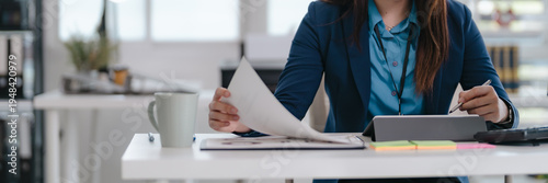 Confident businesswoman sitting at modern office desk reviewing reports and focusing on company tasks