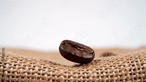 Close up of a single roasted coffee bean hovering above burlap fabric.