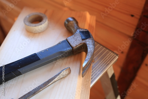The construction equipment is on a metal stepladder. Wooden board, hammer, screwdriver, tape. Summer, spring.