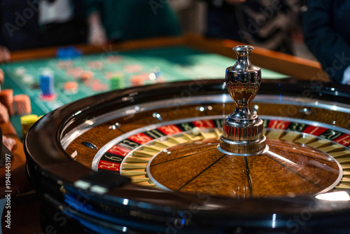 Close view of roulette wheel spinning in casino with players and betting table in background. Gambling, risk and luck concept.