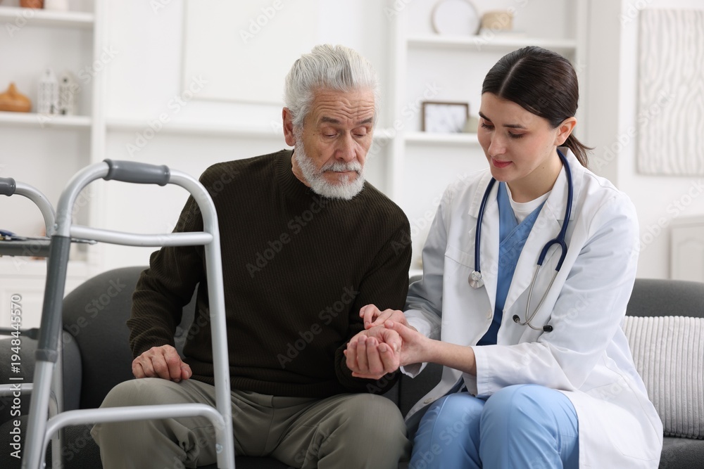 Fototapeta premium Care worker checking senior man's pulse indoors