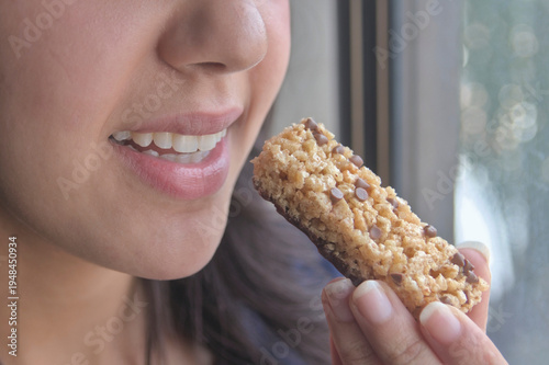 Una joven atleta  comiendo una barra de proteínas como refrigerio.