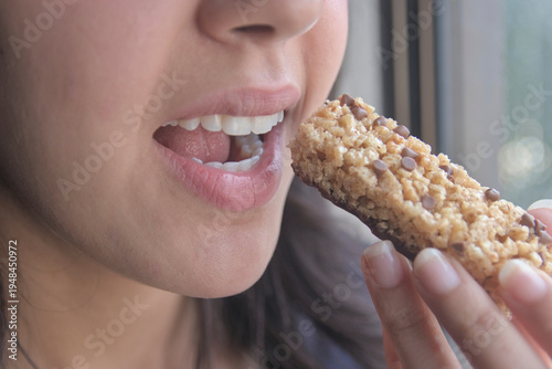 Una joven atleta  comiendo una barra de proteínas como refrigerio.