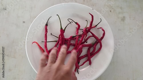 Red chili peppers on a white plate with a hand