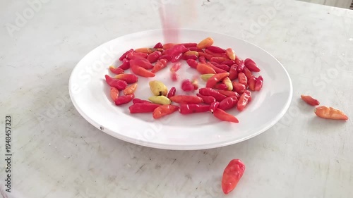 Chili peppers falling onto white plate in slow motion video footage