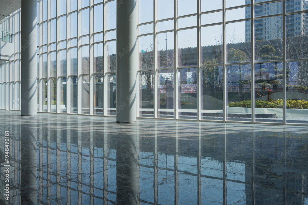Obraz premium Modern architectural interior with glass curtain wall and reflective polished floor capturing urban landscape