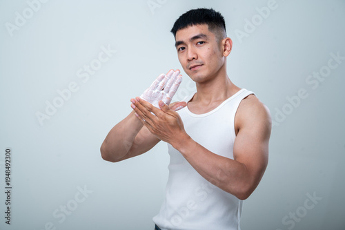 Young Asian man in a white tank top rubs foamy cleanser on his hands against a light gray background, showing personal hygiene, skincare preparation, and daily grooming routine