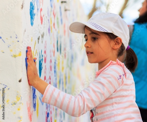 Child Girl Making Colorful Handprints on White Wall Outdoor