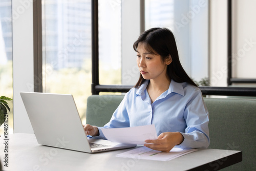 Foto Focused East Asian businesswoman, female office employee sits at coworking desk, analyzing data, preparing report, reviewing documents, working on laptop