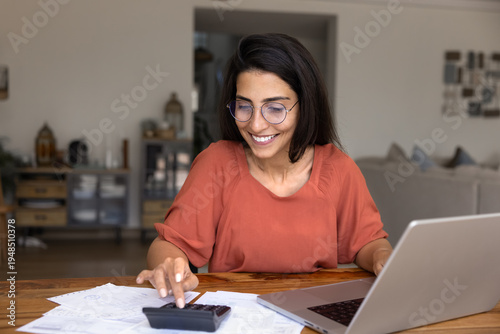 Bild auf Leinwand Smiling young woman in glasses calculate finances at home, using calculator and
