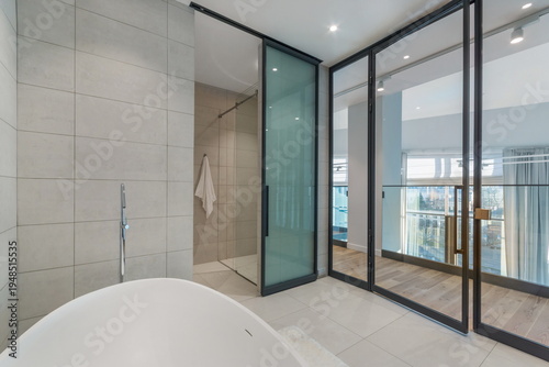 Bathroom with a glass wall in the interior of a luxury mansion. Stylish bath and shower behind a glass partition.