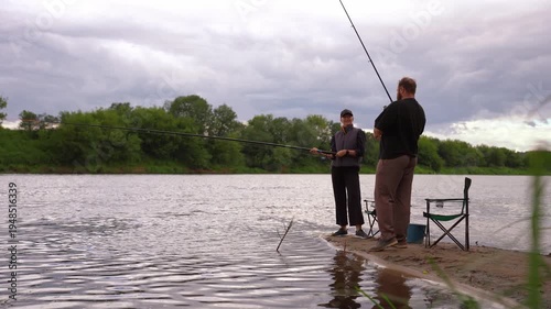 Young couple man and woman fishing on river bank on cloudy day. Spending time together. Relaxing family holidays by the river.
