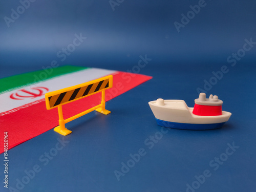 A toy ship facing a yellow construction barrier with iran flag on a blue background