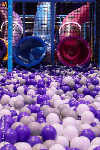Colorful slides leading into a vast purple, white, and grey ball pit at a modern indoor playground, offering a fun and safe recreational space for children's physical activity and sensory play.