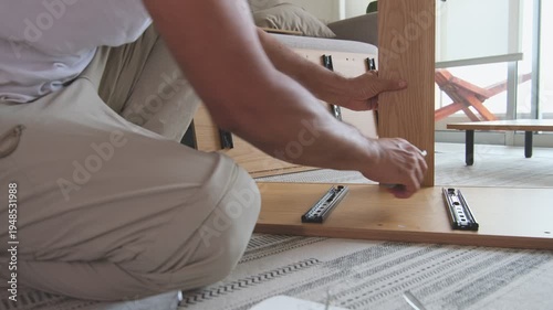 Unrecognizable handyman assembling new flat pack wooden furniture using a screwdriver at home