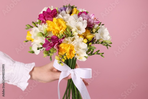 Woman with bouquet of beautiful freesia flowers on pink background, closeup