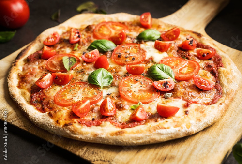 Fresh homemade pizza topped with mozzarella cheese, tomatoes, basil and oregano served on a wooden board