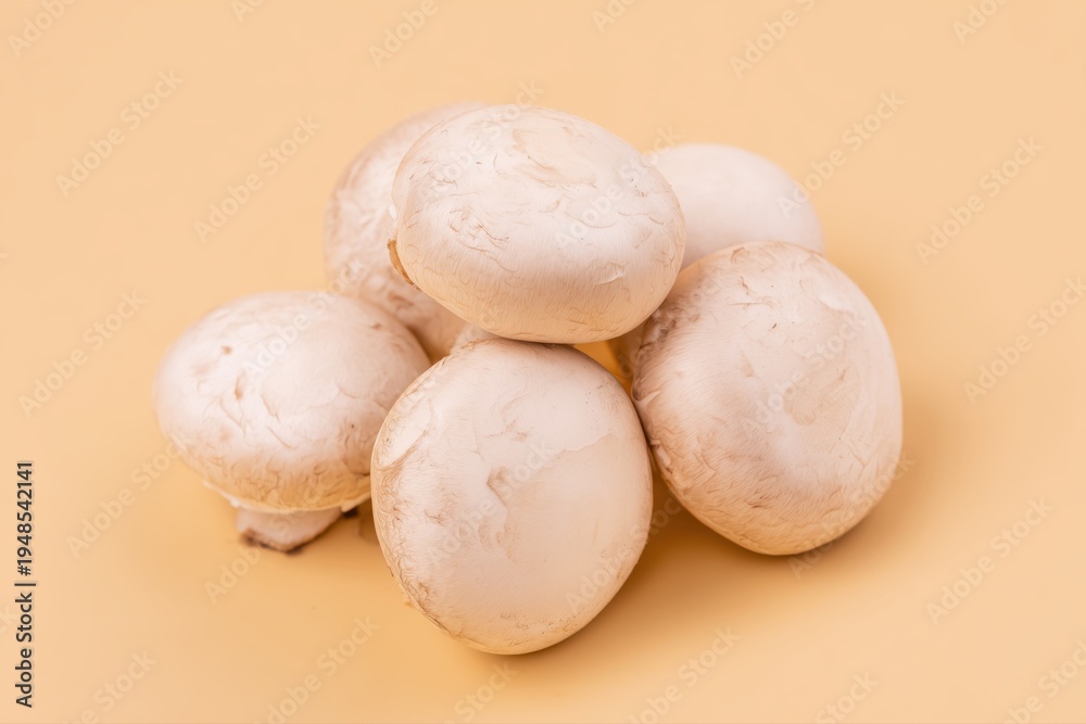 Fototapeta premium Fresh whole white button mushrooms grouped on a warm beige background, soft lighting, minimal shadow, clean composition.