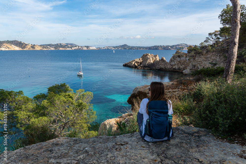 Fototapeta premium Woman with Backpack Enjoying the Scenic View over Cala Fornells Bay in Mallorca