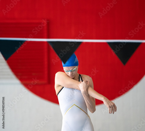Female swimmer warms up before the start in the swimming pool against the background of the red sun 
