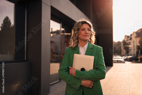 Businesswoman holding laptop standing in city at sunset
