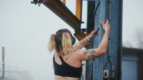 Tattooed Athletic Woman Doing Pull-Ups on Industrial Metal Ladder at Harbor Waterfront