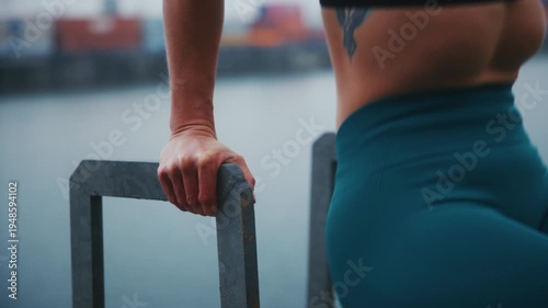 Tattooed Athletic Woman Doing Tricep Dips on Parallel Bars at Industrial Harbor Waterfront