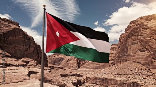 The national flag of Jordan proudly waves against a backdrop of ancient desert mountains.