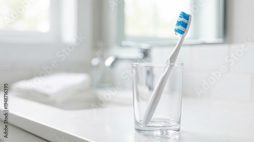 Modern white toothbrush in glass. A white toothbrush with blue bristles in a clear glass on a bathroom counter