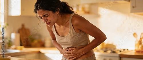 Woman stomach pain abdominal cramp female discomfort home kitchen morning light casual clothing health problem digestive issue menstruation pain stress young adult cramps discomfort indoor sunlight
