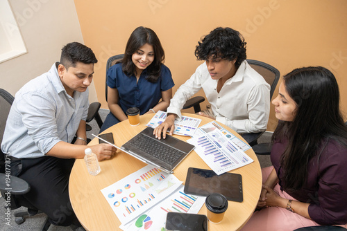 Young indian asian business team entrepreneur meeting in office, discussing company sales reports and financial graphs on a laptop and paper documents, teamwork and professional collaboration.