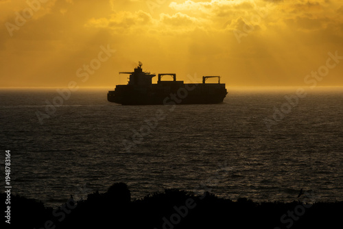 Silhouette of a container or tanker ship on the ocean at sunrise or sunset