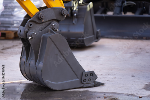 Foto Compact excavator digging bucket resting on concrete at an equipment yard, repre