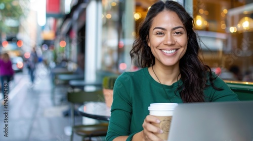 Happy young woman enjoying coffee and working on laptop at outdoor cafe in urban setting with vibrant atmosphere and soft sunlight