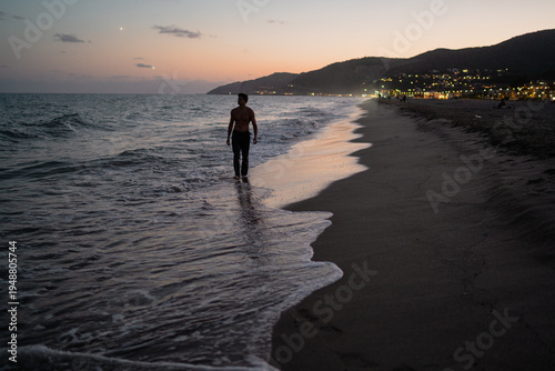 Foto Young blond muscular man walking barefoot on beach at dusk