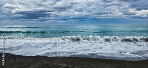 Beach scene with waves under cloudy sky over coastal seashore horizon