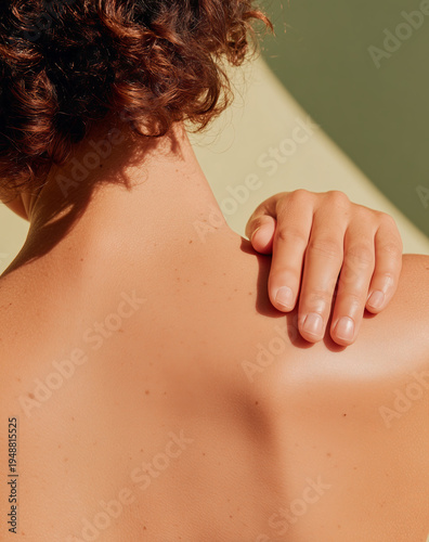 Sunlit close-up of a woman's hand touching her glowing back and shoulder