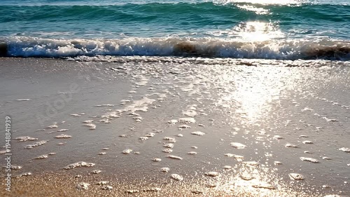 Sunlight reflects on wet sandy beach with approaching wave and footprints