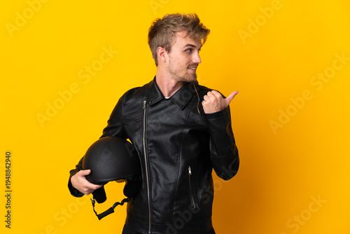Man with a motorcycle helmet isolated on yellow background pointing to the side to present a product