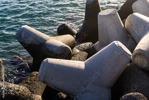 Фотография Concrete breakwater structures arranged on rocky shoreline with water gently lap